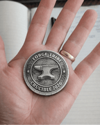 Hand holding a silver coin with 'Forge Tribe Crucible 2026' design in front of a keyboard.